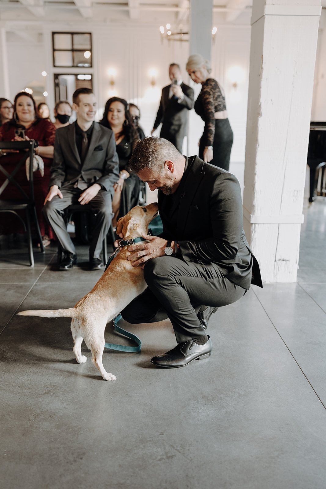 Groom greeting dog at end of wedding aisle