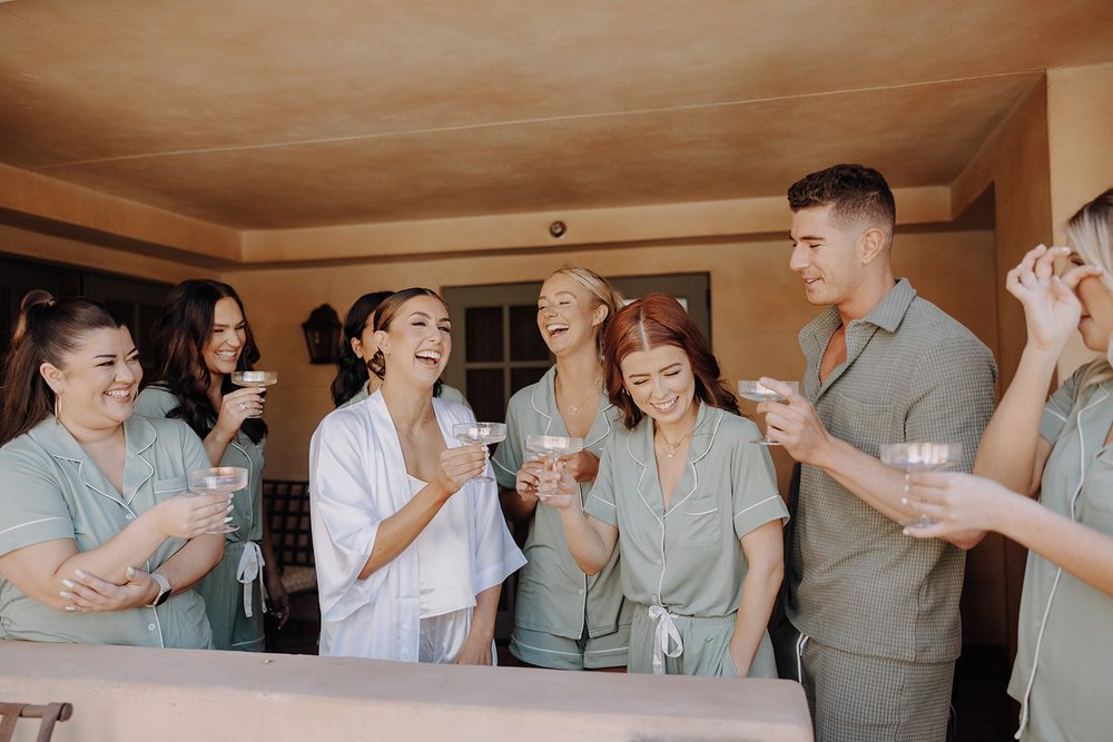 Bride drinks champagne while getting ready with bridal party