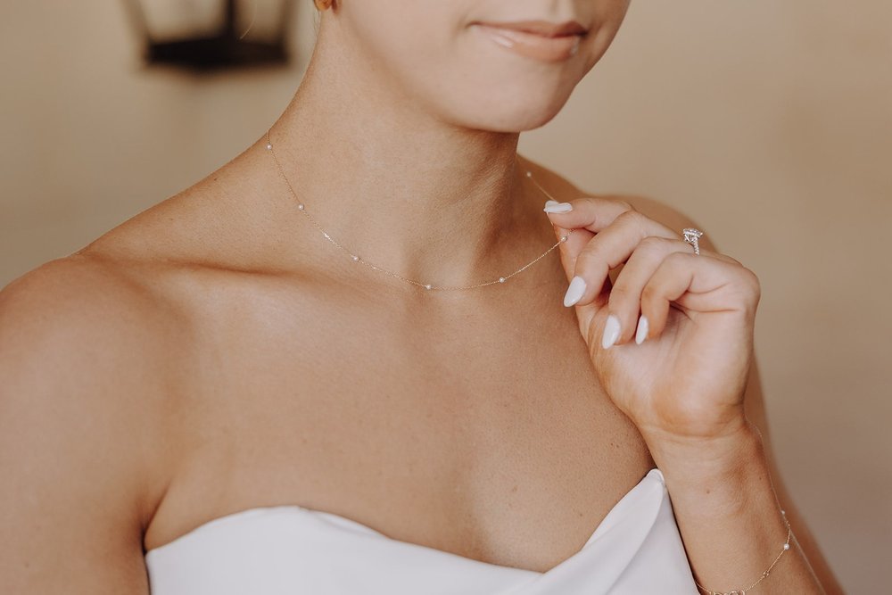 Bride plays with delicate gold chain with mini pearls while getting ready for her luxury resort wedding in Arizona