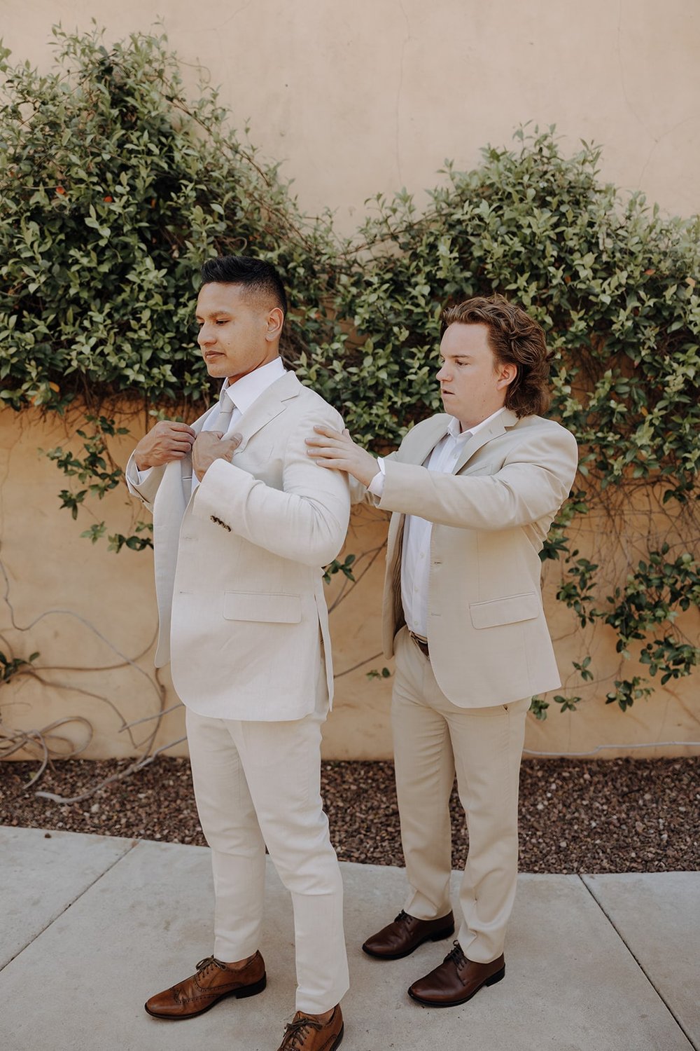 Groom gets helped into beige suit while getting ready for luxury resort wedding in Arizona