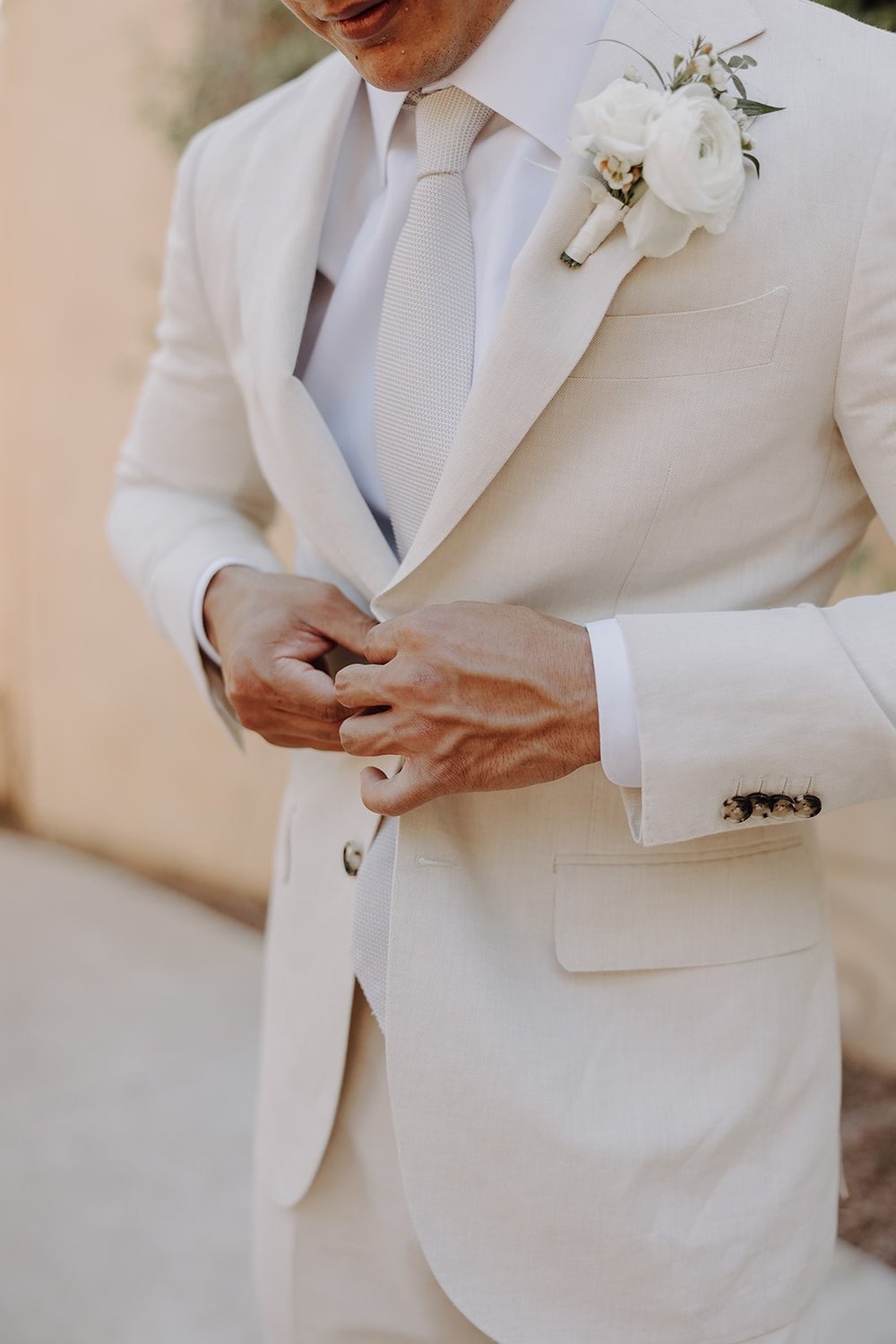 Groom buttons beige suit while getting ready for luxury resort wedding at Royal Palms Resort &amp; Spa