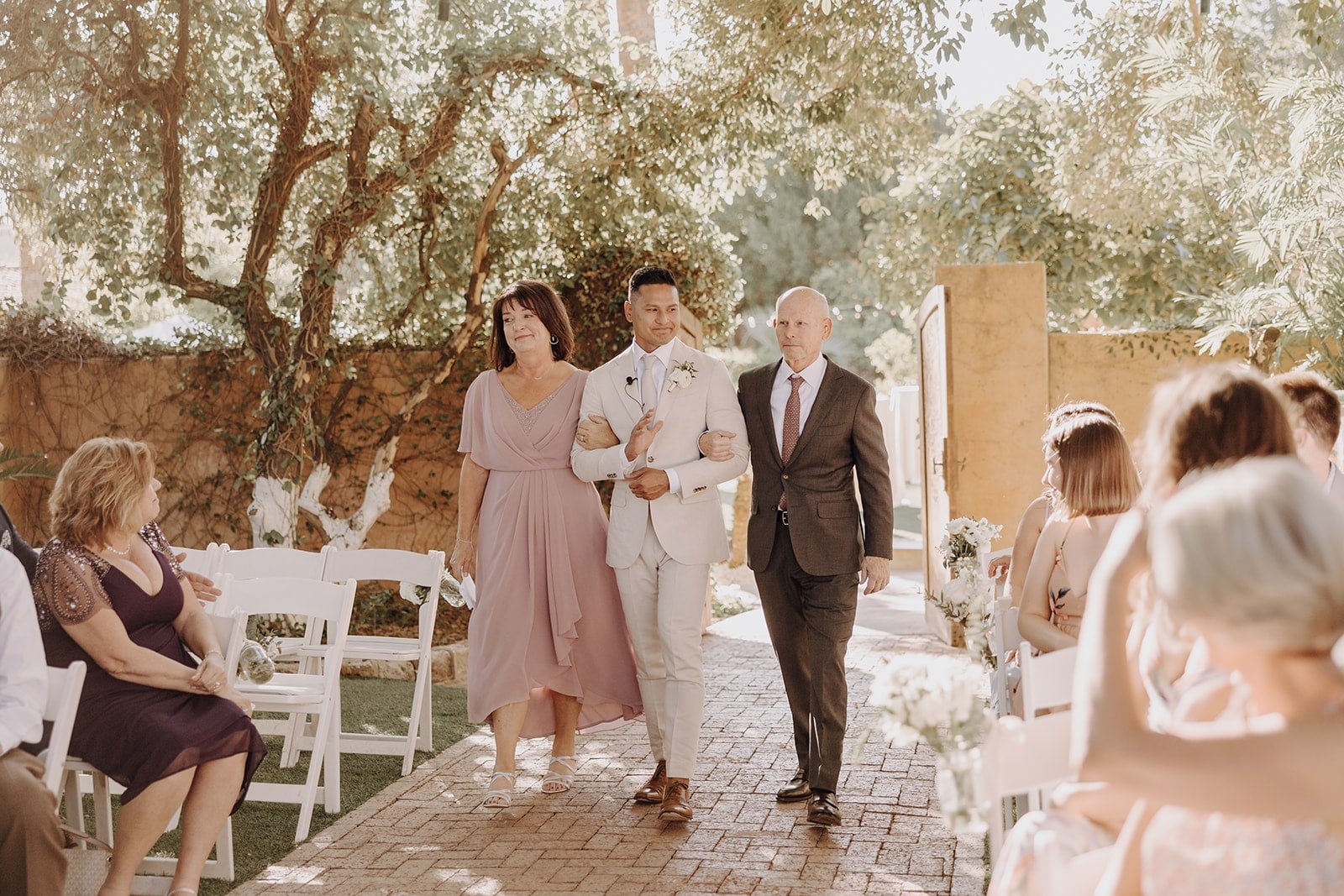 Groom enters outdoor wedding ceremony with his parents