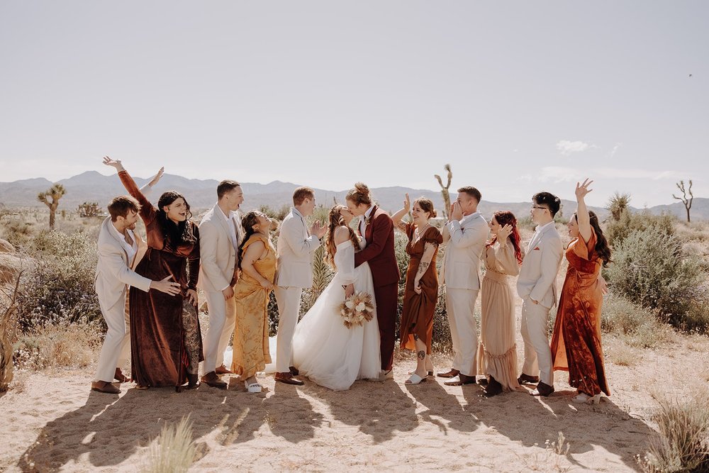 Wedding party cheers while bride and groom kiss during Joshua Tree wedding photos