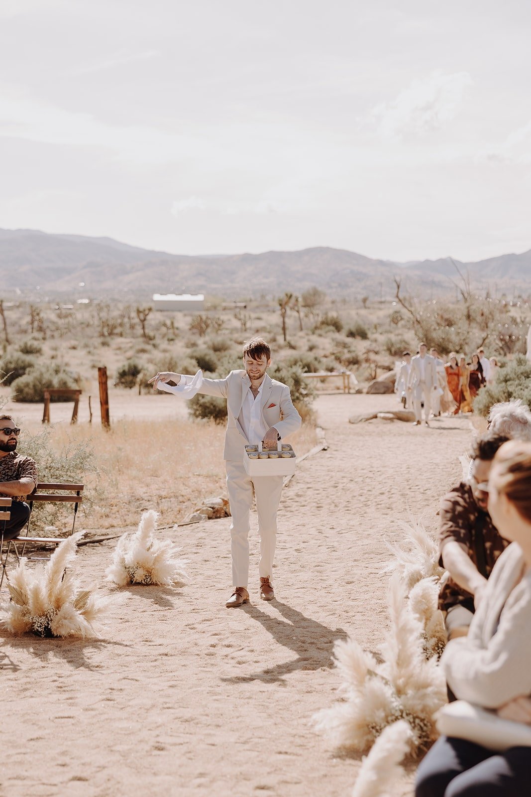 Groomsman passes out cans of beer at outdoor wedding ceremony at The Ruin Venue in Joshua Tree