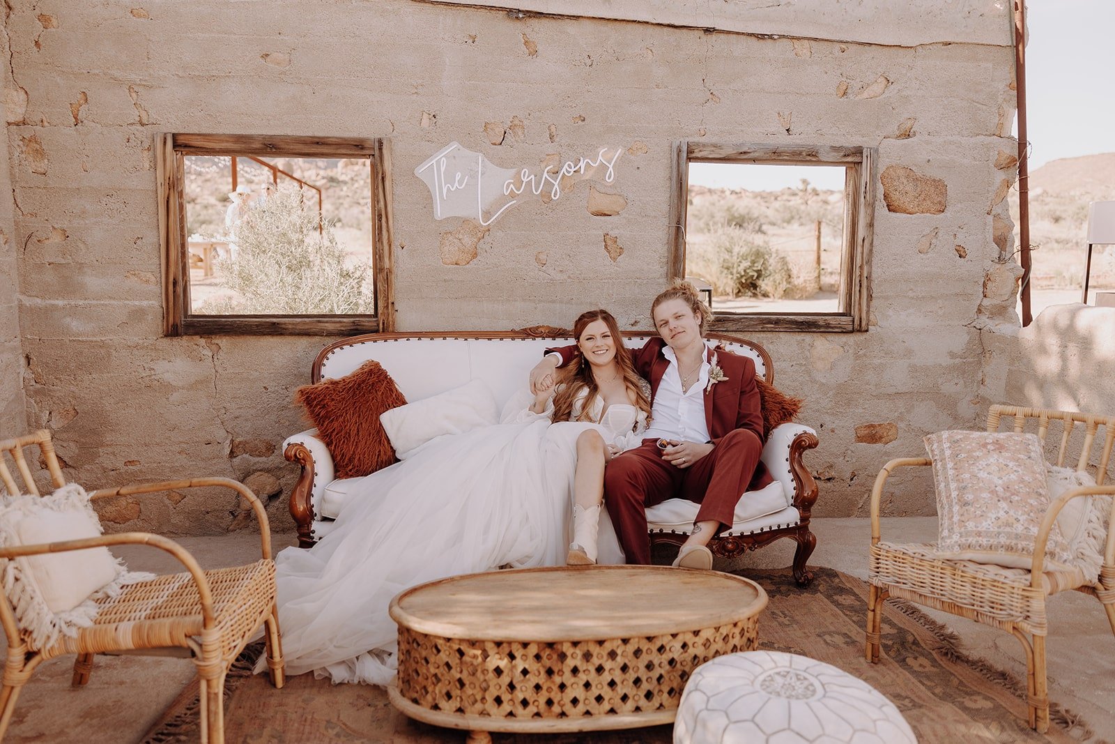 Bride and groom sit on white couch at The Ruin Venue after their outdoor wedding ceremony in Joshua Tree