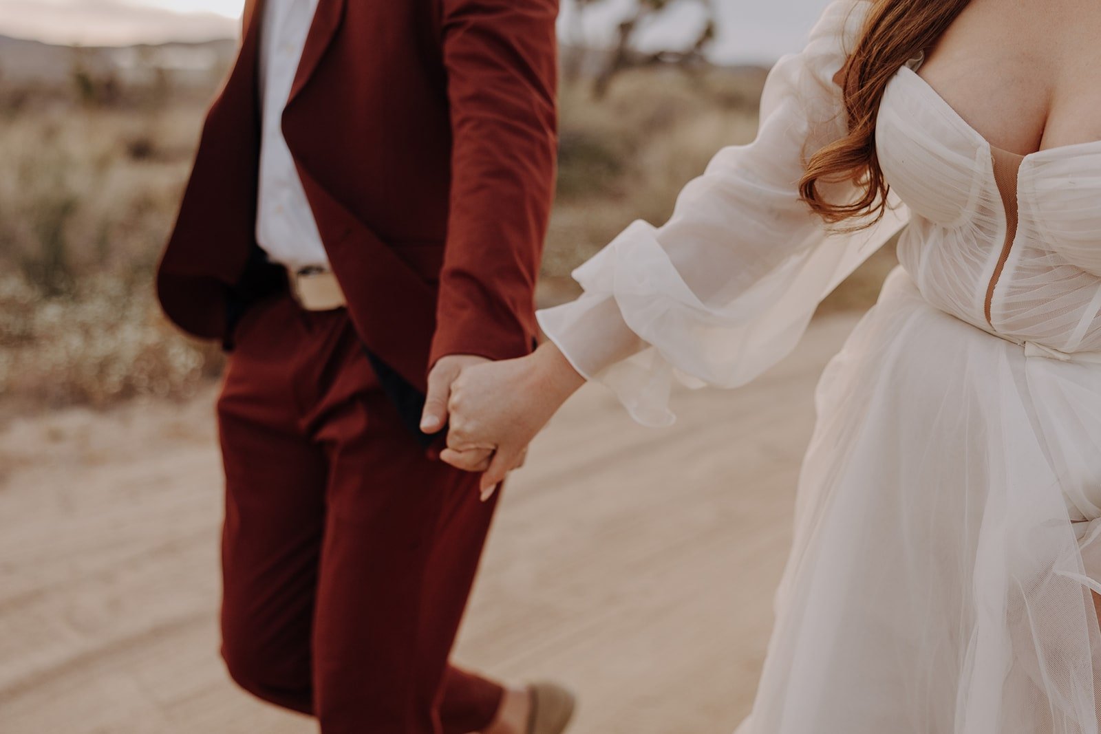 Bride and groom hold hands while walking down the road after their Joshua Tree wedding
