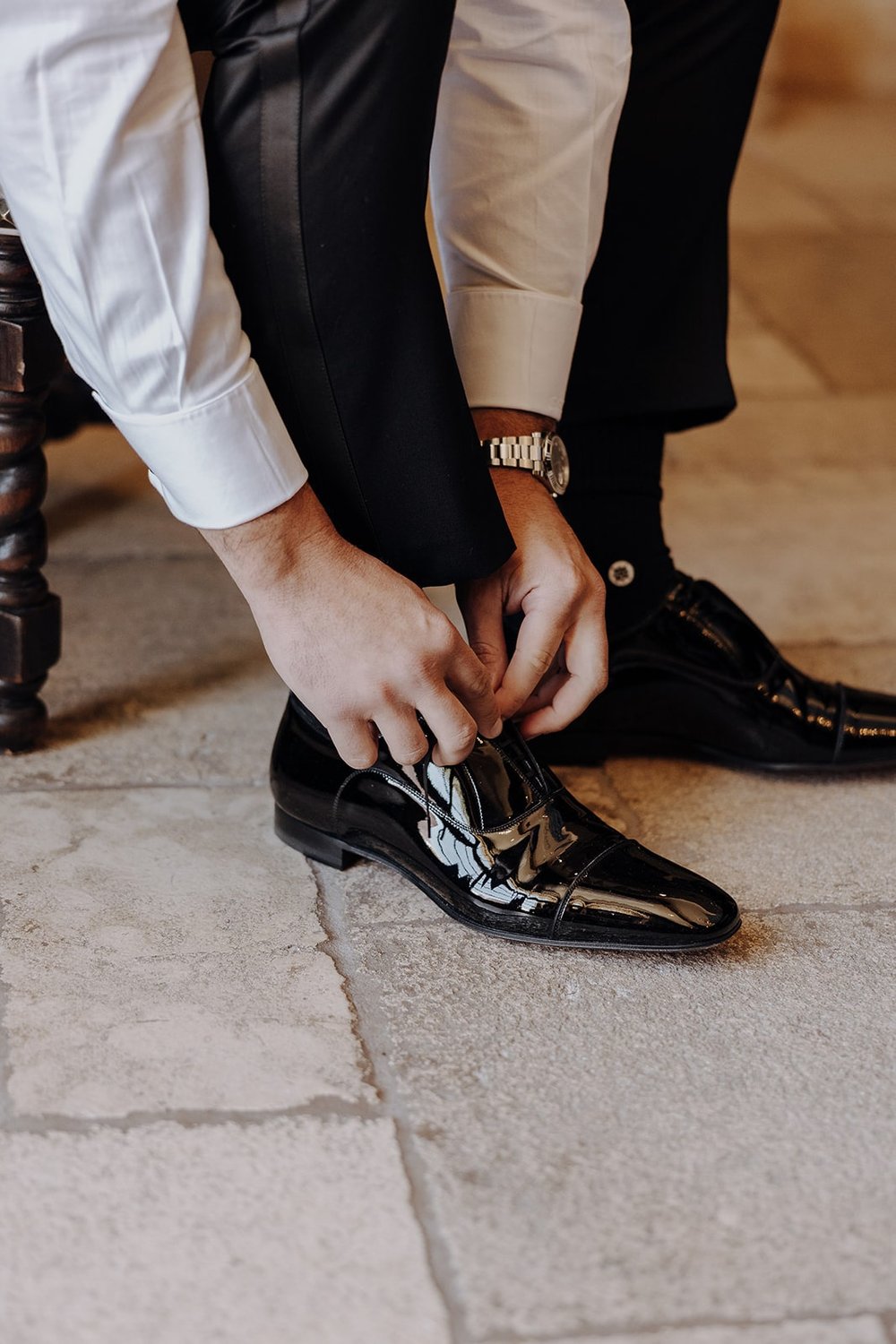 Groom ties his Christian Louboutin patent leather shoes while getting ready for luxury wedding in California