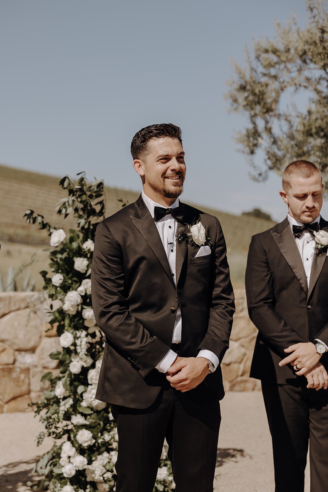 Groom standing at the end of the wedding aisle in a black tuxedo