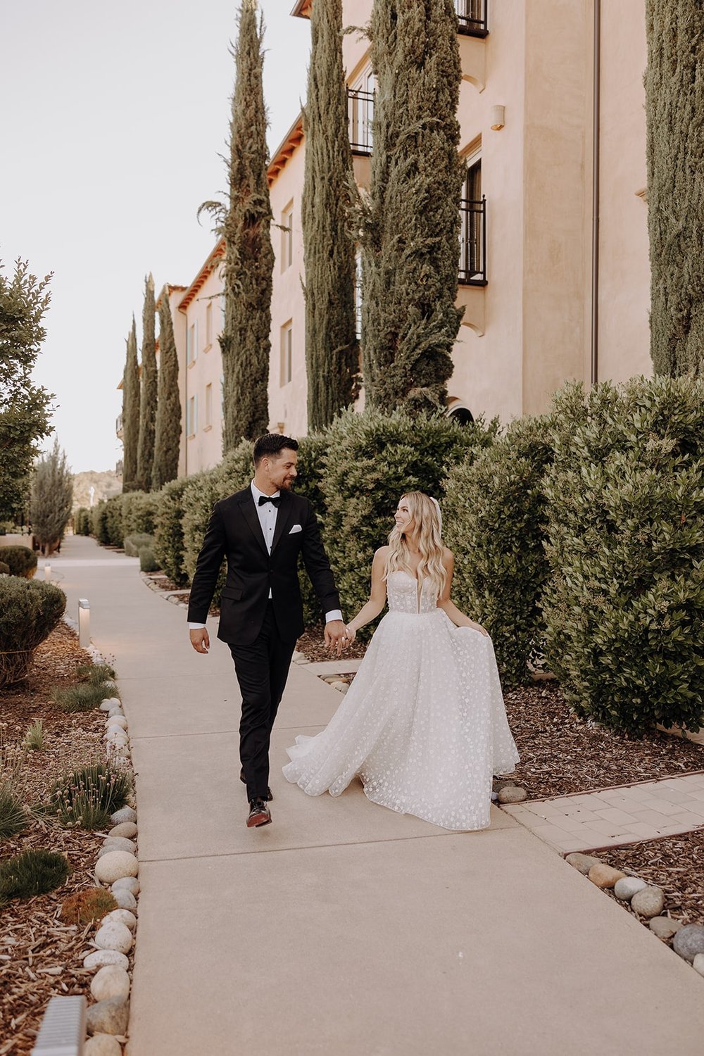 Bride and groom hold hands while walking around Allegretto Vineyard Resort during their luxury wedding 