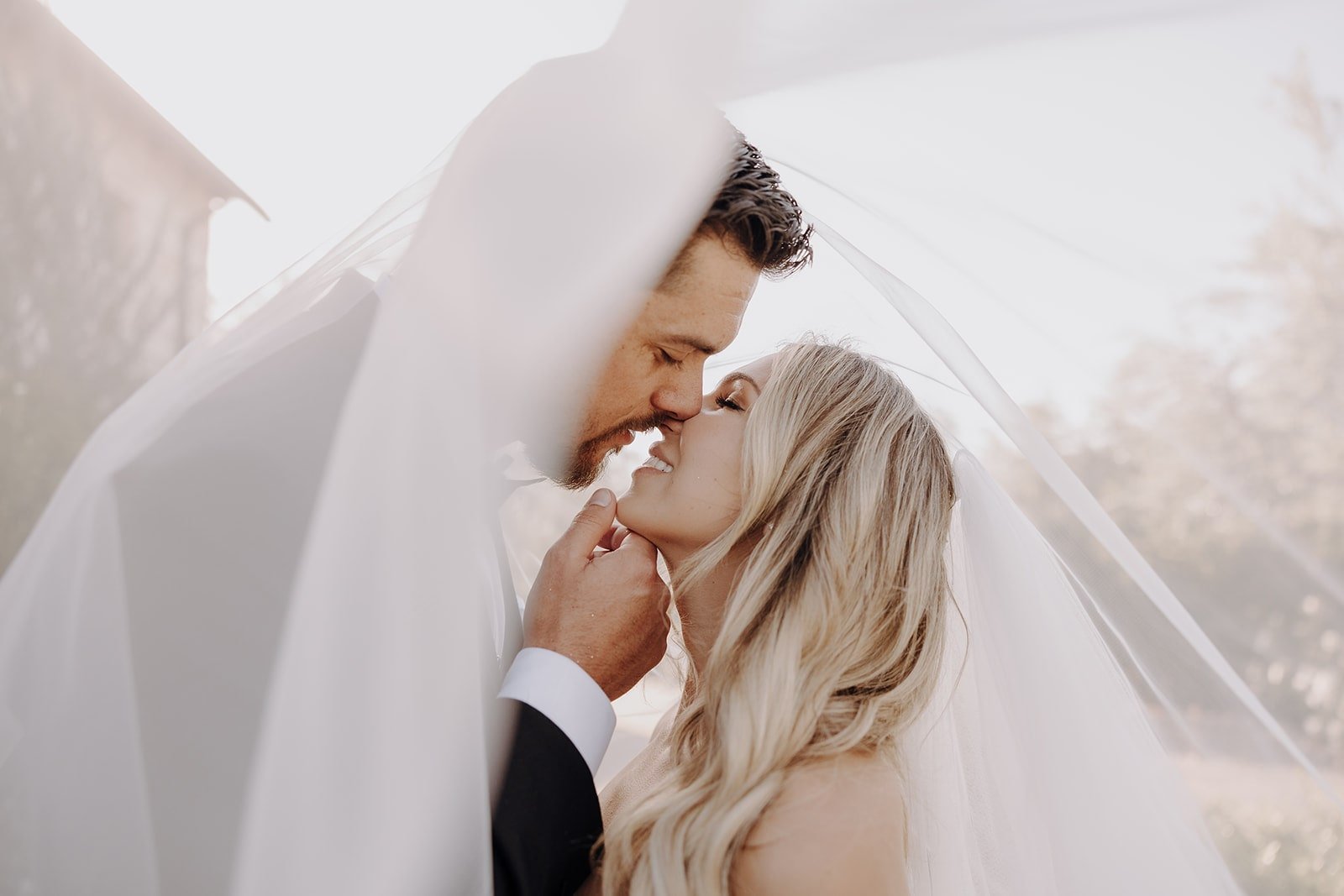 Bride and groom kiss under the veil during luxury wedding photos