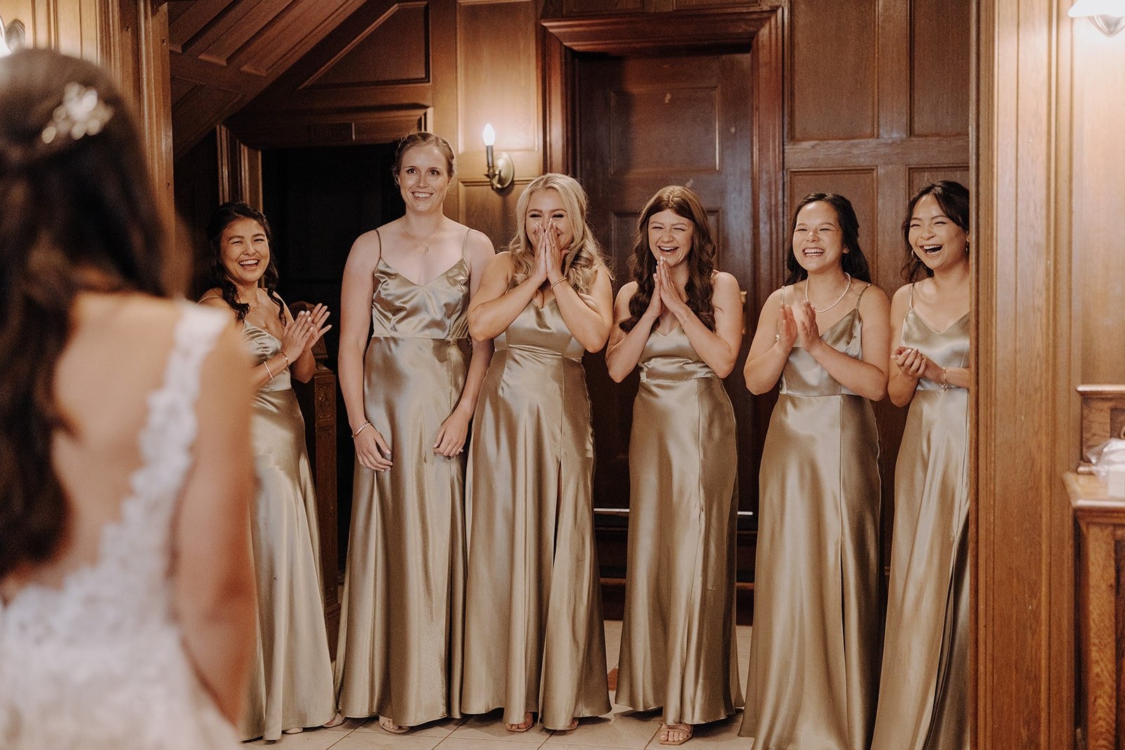 Bridesmaids wearing champagne colored dresses react to first look with the bride