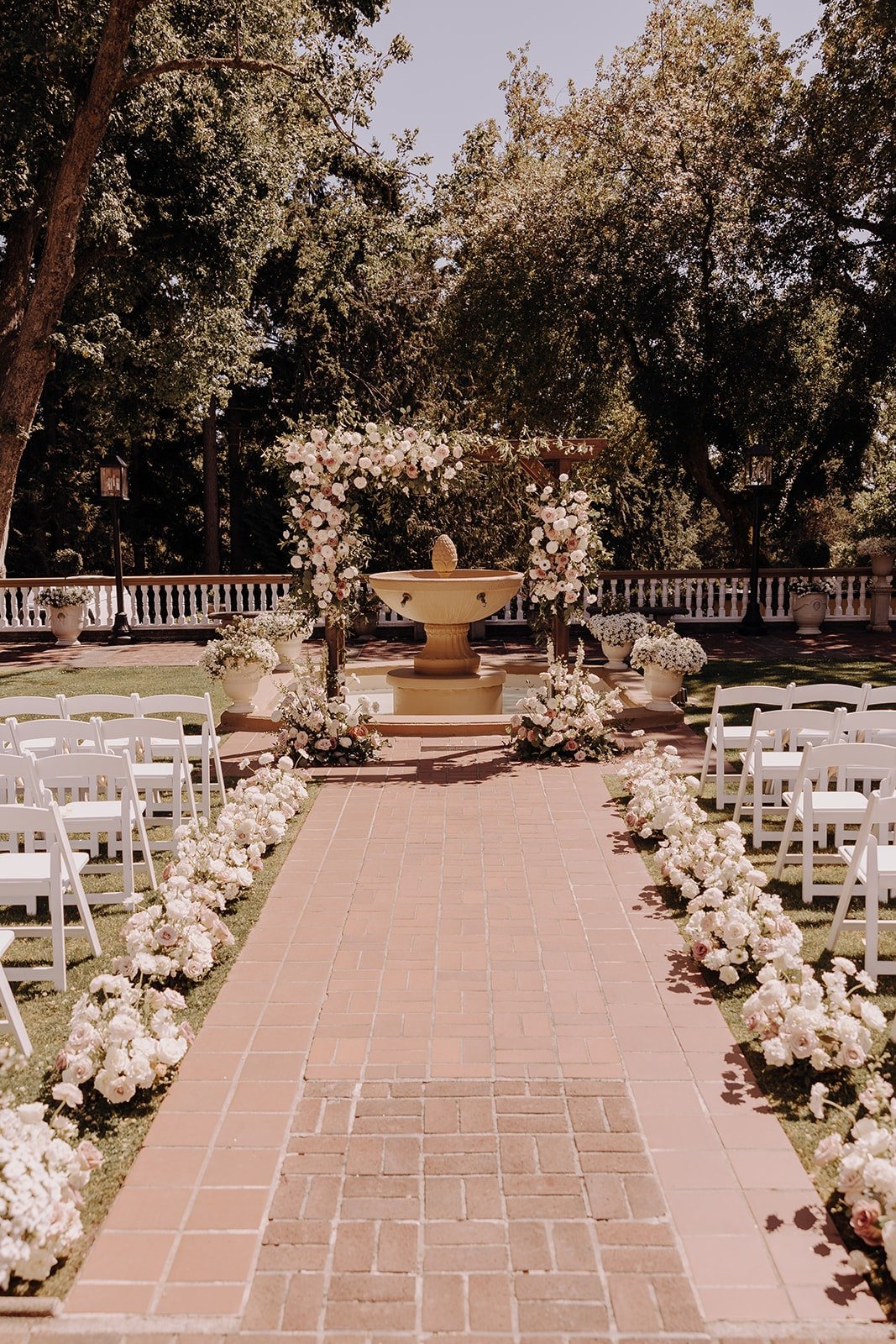 White chairs and flowers with fountain and floral arch at outdoor wedding ceremony at Lairmont Manor