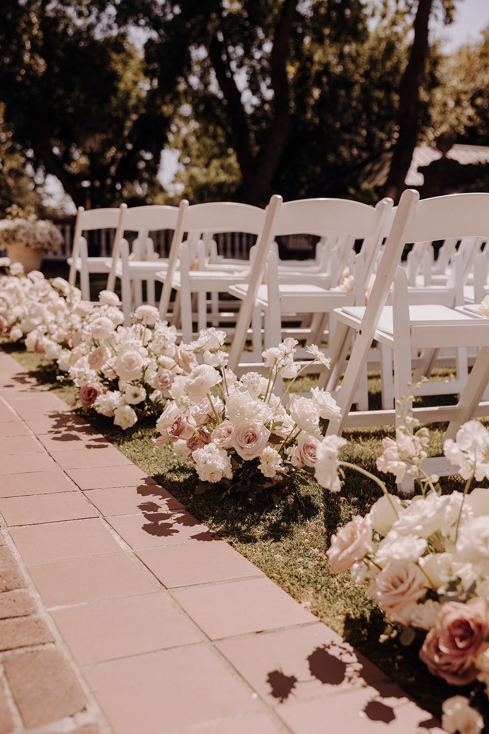 White wood chairs and white floral bouquets at outdoor wedding ceremony