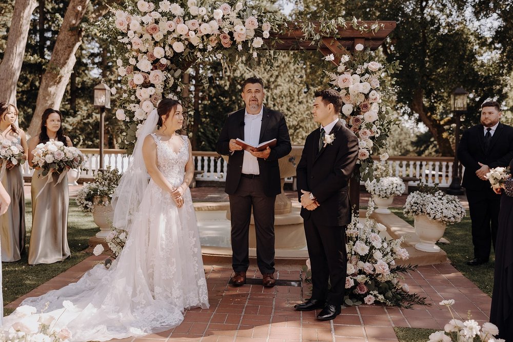 Bride and groom stand under a floral arch at their Washington wedding ceremony at Lairmont Manor