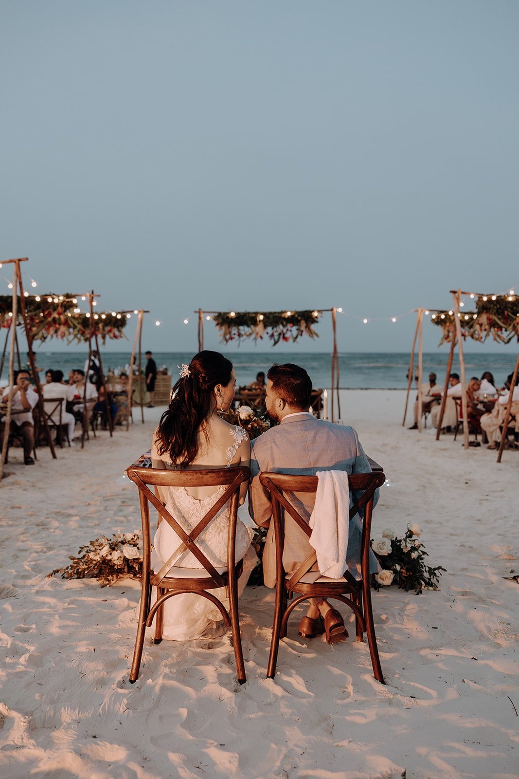 Bride and groom sit at their sweetheart table on the beach at their Dreams Royal Beach Punta Cana wedding