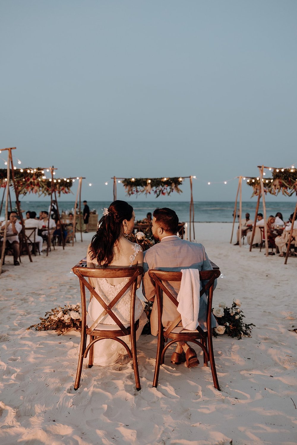 Bride and groom sit at their sweetheart table on the beach at their Dreams Royal Beach Punta Cana wedding