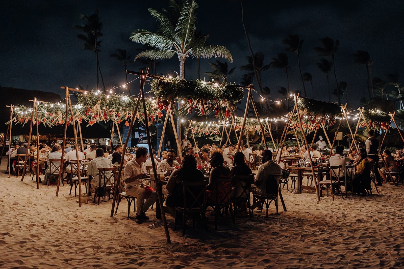 Guests sit under string lights on the beach during the Dreams Royal Beach Punta Cana wedding reception