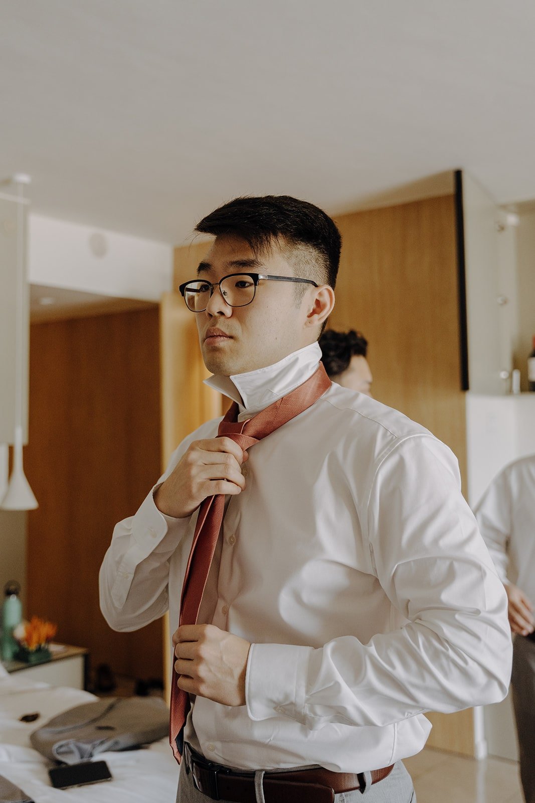 Groom adjusts his burnt orange tie while getting ready for his resort wedding in Mexico