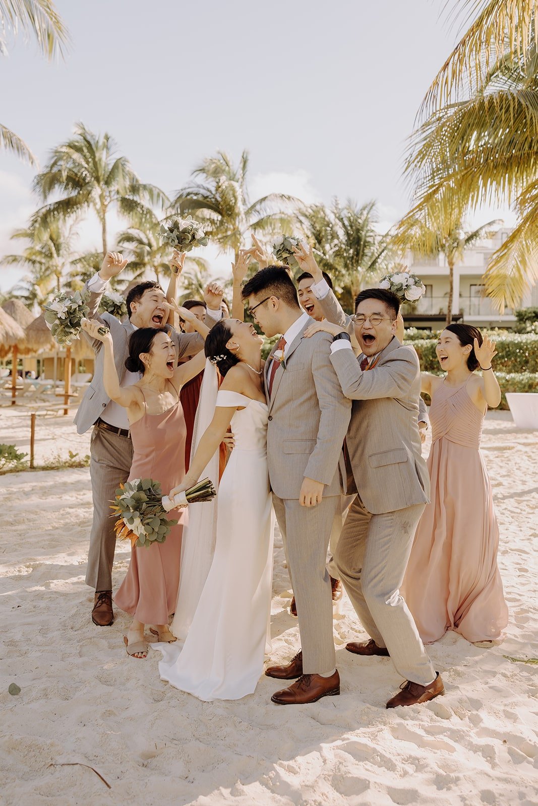 Bride and groom kiss while their wedding party celebrates in the background at their destination wedding in Mexico