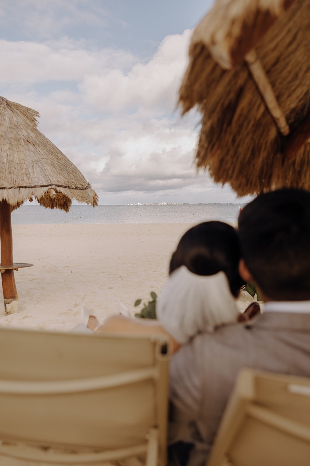 Bride and groom recline on lounge chairs on the beach before their wedding ceremony