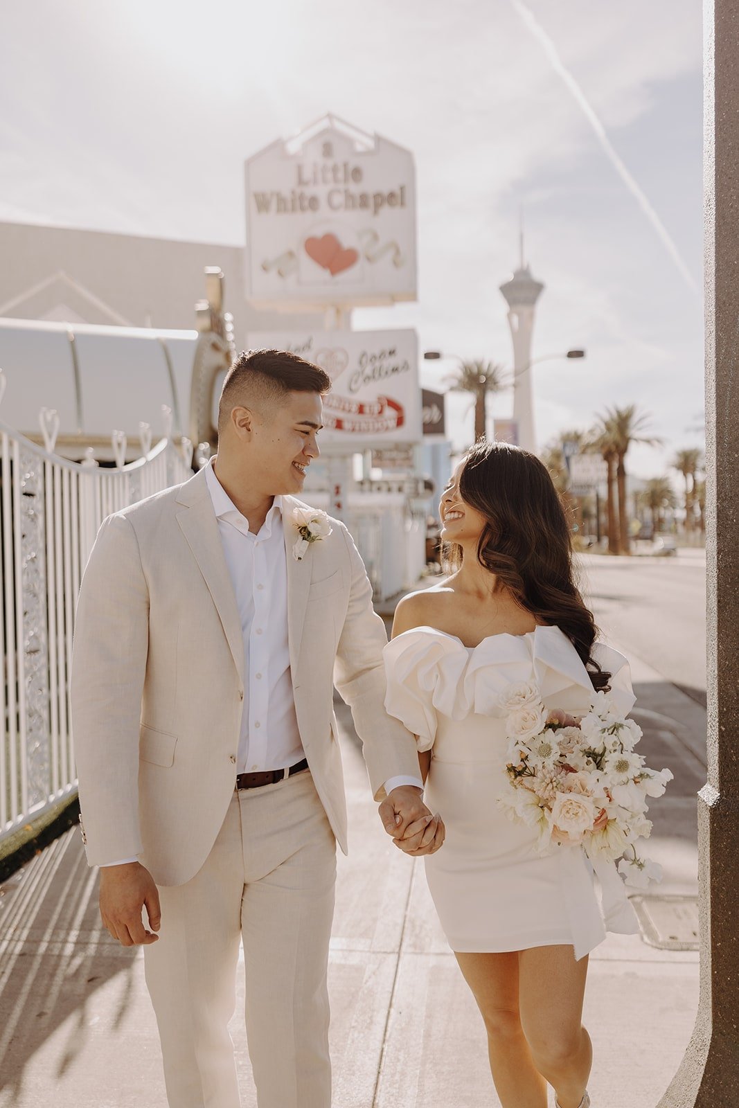 Bride and groom hold hands and walk in front of the Little White Chapel in Vegas