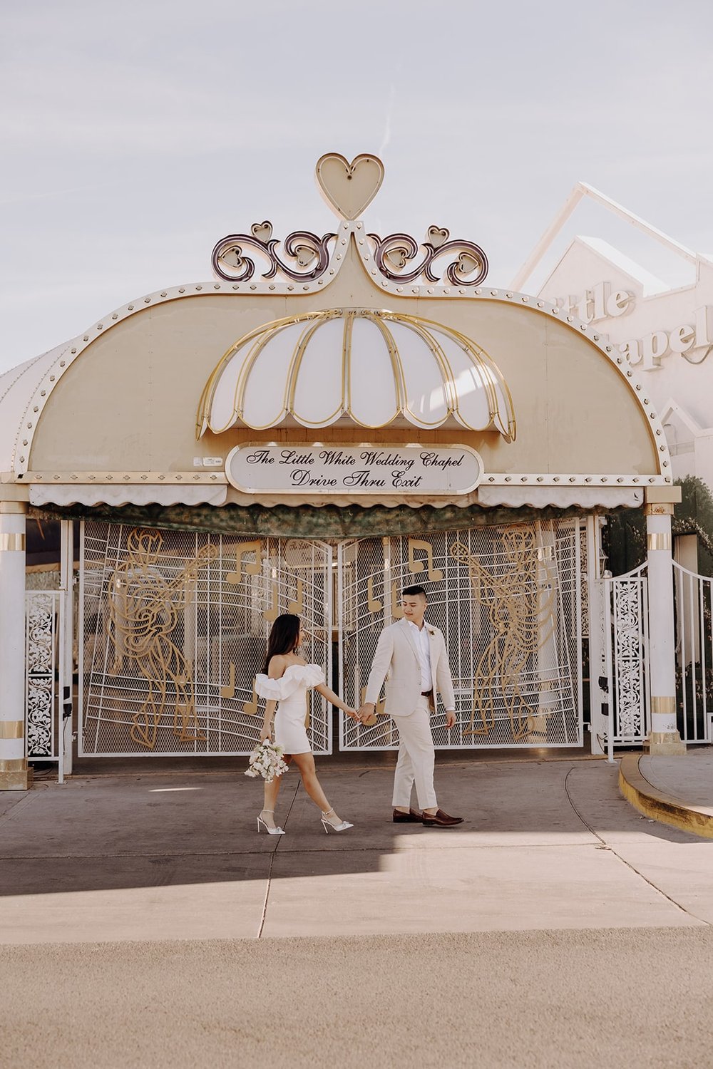 Bride and groom hold hands while walking in front of the Little White Chapel in Las Vegas