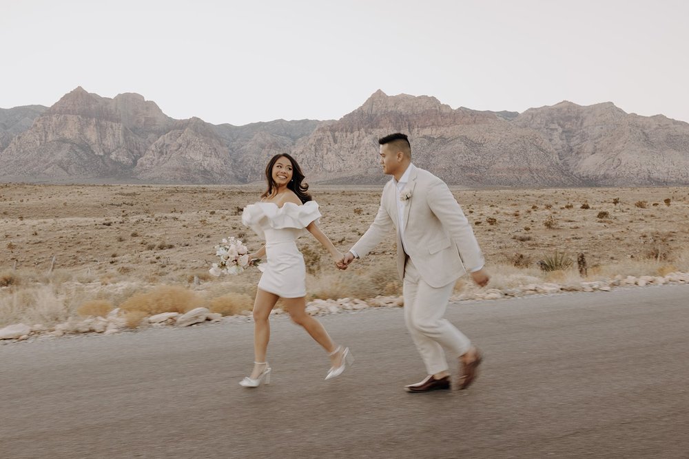 Bride and groom hold hands and run through the street at their Red Rock Canyon elopement