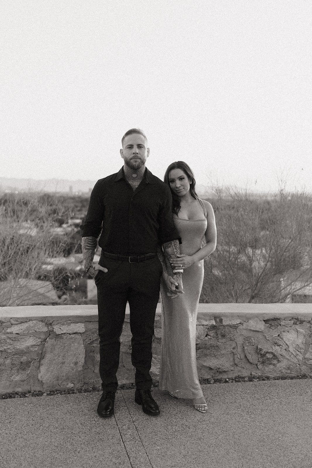 A man and woman stand outdoors holding hands; the woman leans her head on the man's shoulder for their luxury engagement photos