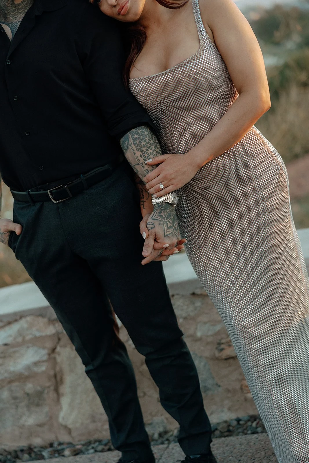 A man and woman stand outdoors holding hands; the woman leans her head on the man's shoulder for their luxury engagement photos