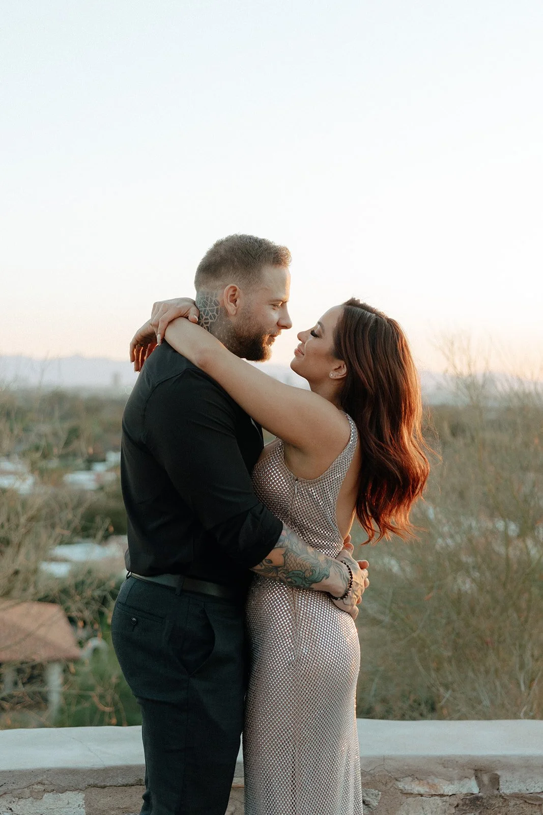 A man and woman stand outdoors holding hands; the woman leans her head on the man's shoulder for their luxury engagement photos