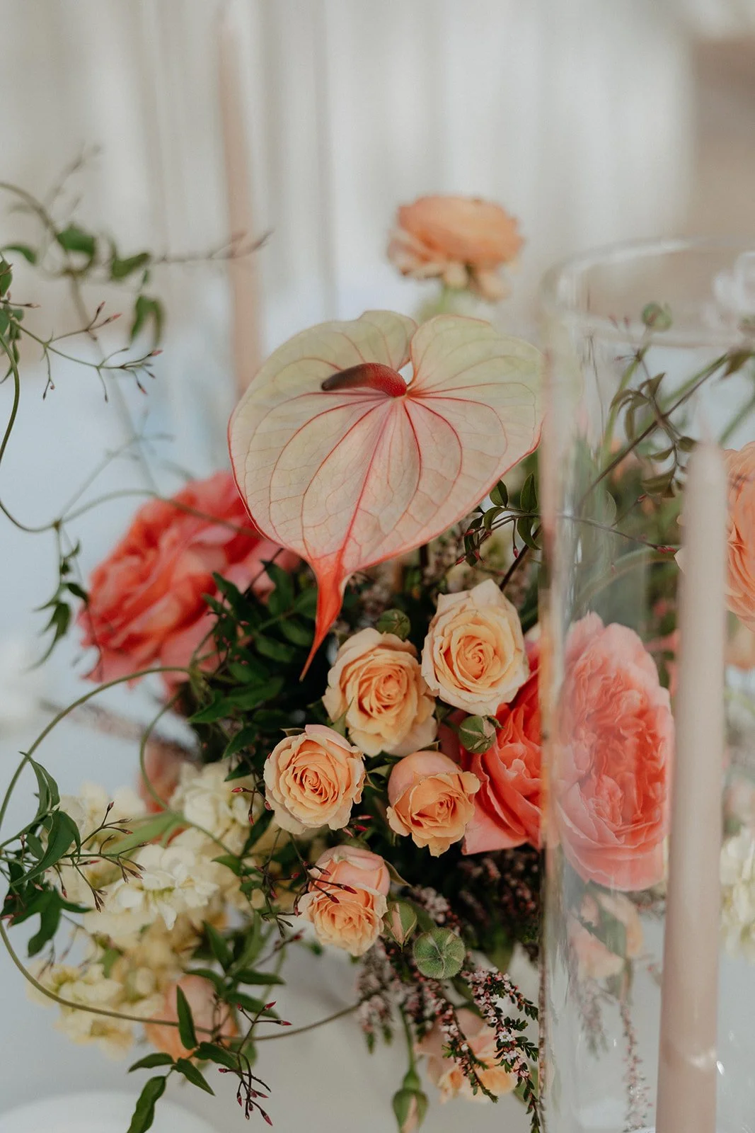 Elegant outdoor dining table set with white linens, glassware, and floral arrangements; a large green and peach flower arch decorates the fireplace in the background for a destination tropical wedding