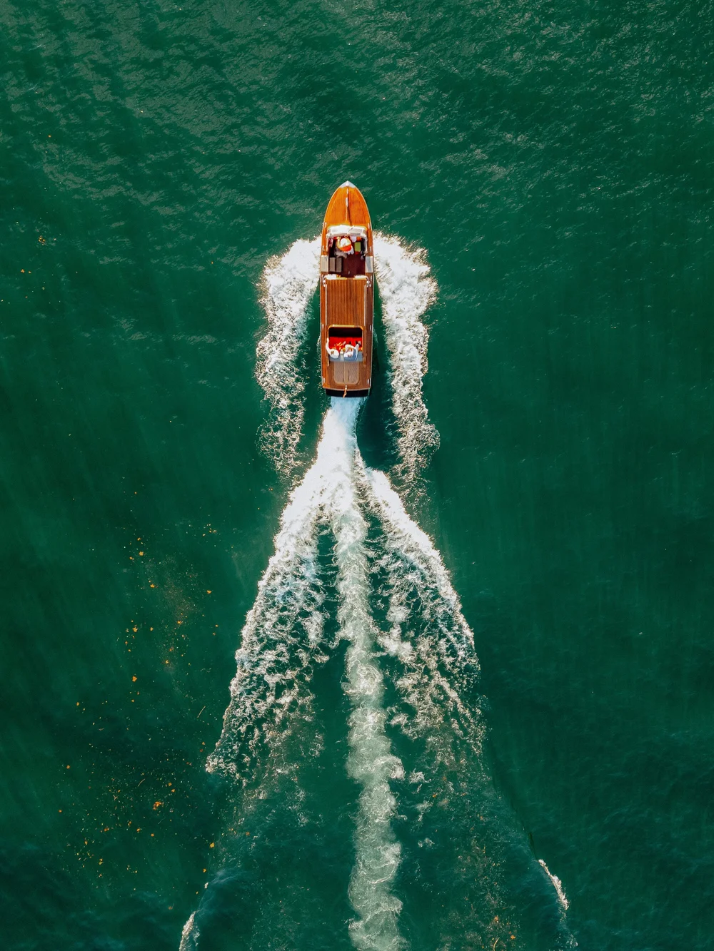 A boat moves through green water, leaving a white wake trail behind it, viewed from above.