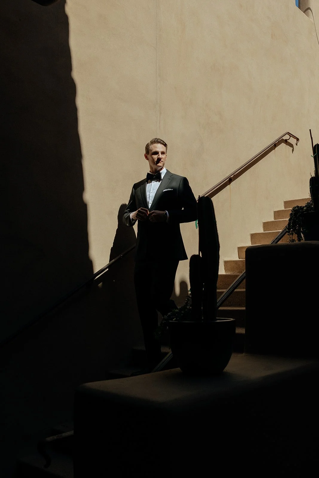 A bride in a white gown holding a bouquet stands next to a groom in a black suit and bow tie in a corridor with tan walls and wooden beams for a destination wedding in Italy