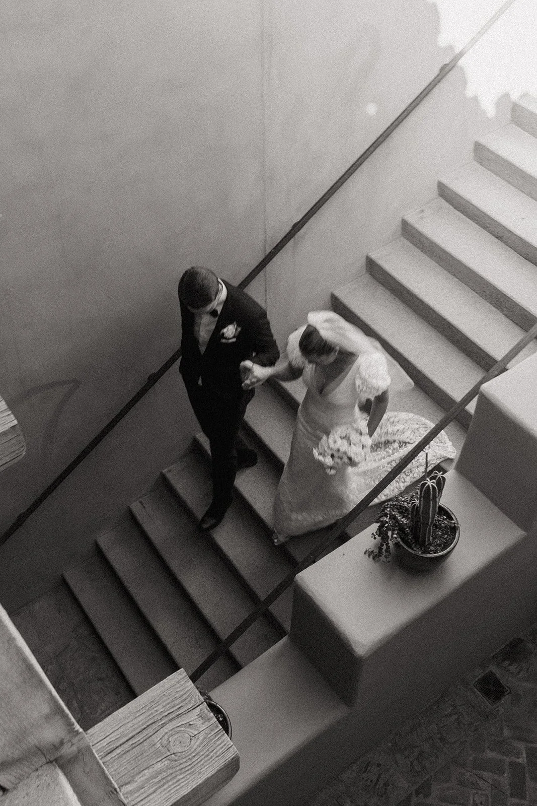 A bride in a white gown holding a bouquet stands next to a groom in a black suit and bow tie in a corridor with tan walls and wooden beams for a destination wedding in Italy