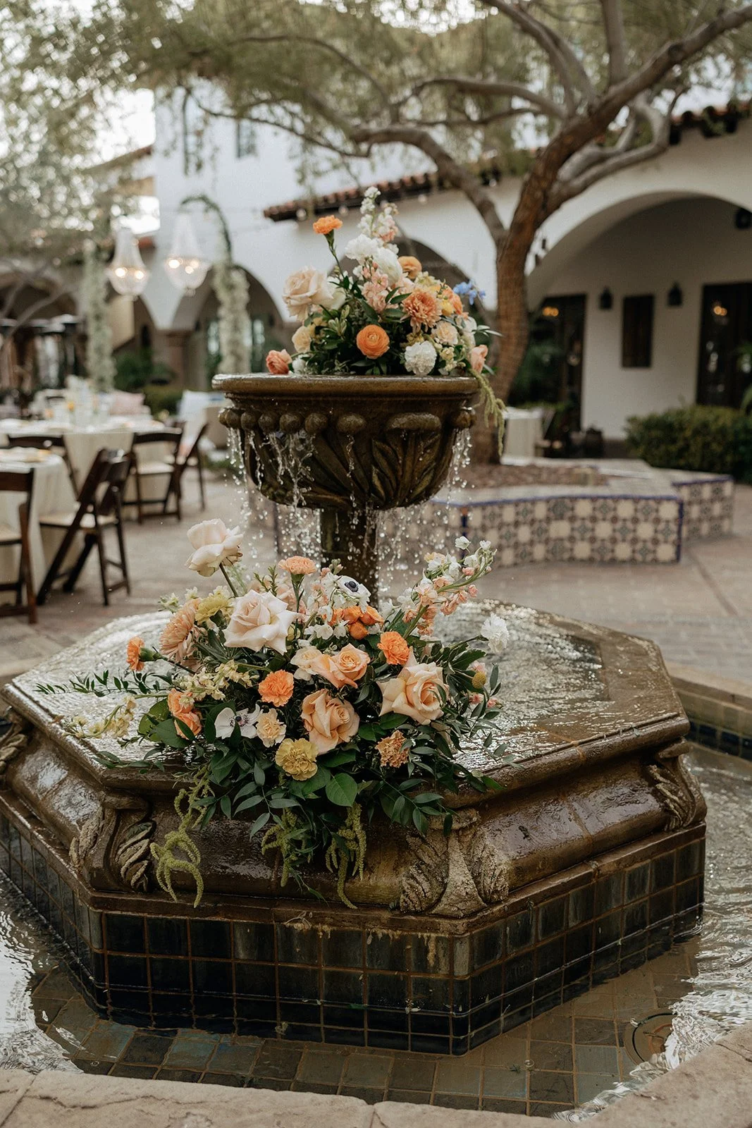 Outdoor courtyard with round tables set for an event, white tablecloths, wooden chairs, and candlelit centerpieces under large trees for an Italy destination wedding 