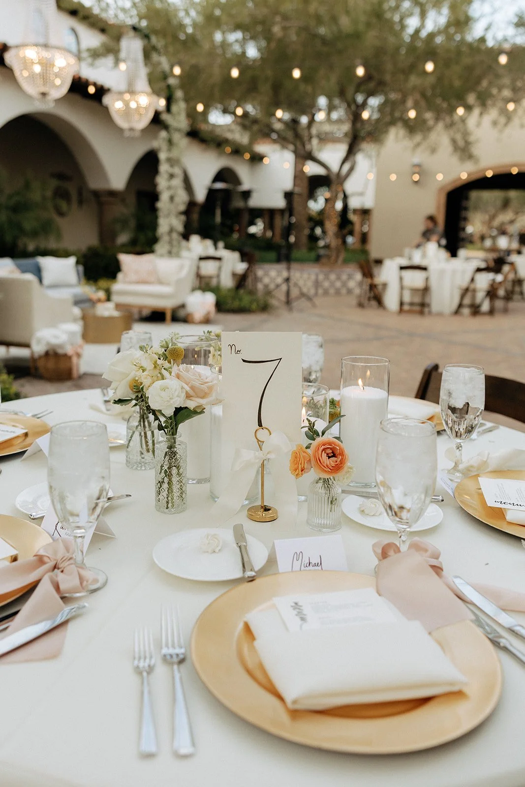 Outdoor courtyard with round tables set for an event, white tablecloths, wooden chairs, and candlelit centerpieces under large trees for an Italy destination wedding 