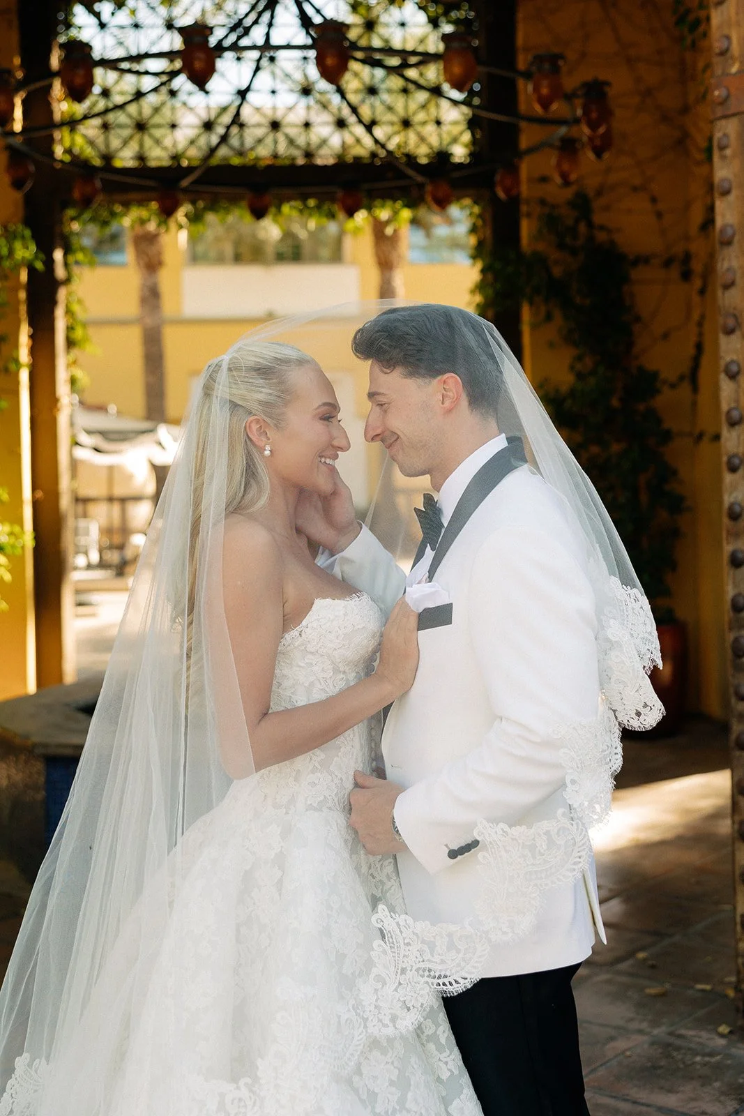 A bride and groom in wedding attire stand close together, smiling at each other under a decorated outdoor pavilion for a luxury wedding