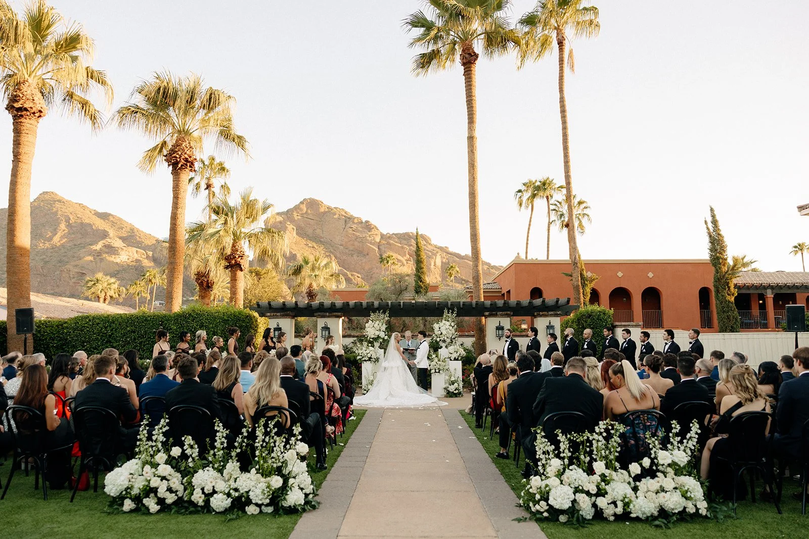 Outdoor wedding ceremony with seated guests, floral arrangements, and mountain scenery in the background under a clear sky for a luxury wedding