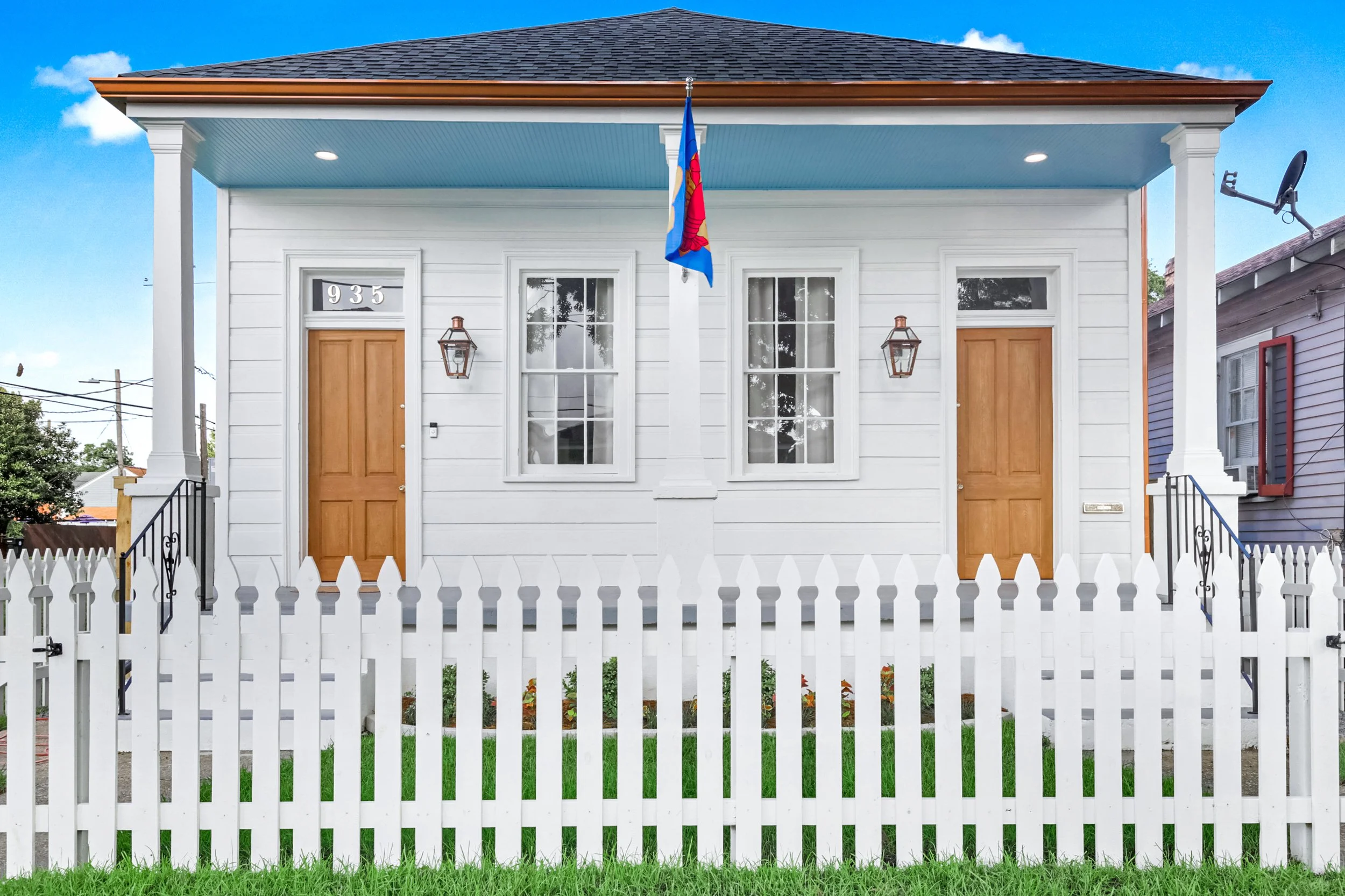 Fully renovated historic New Orleans cottage with restored porch, wood doors, traditional columns, and fresh exterior finishes.