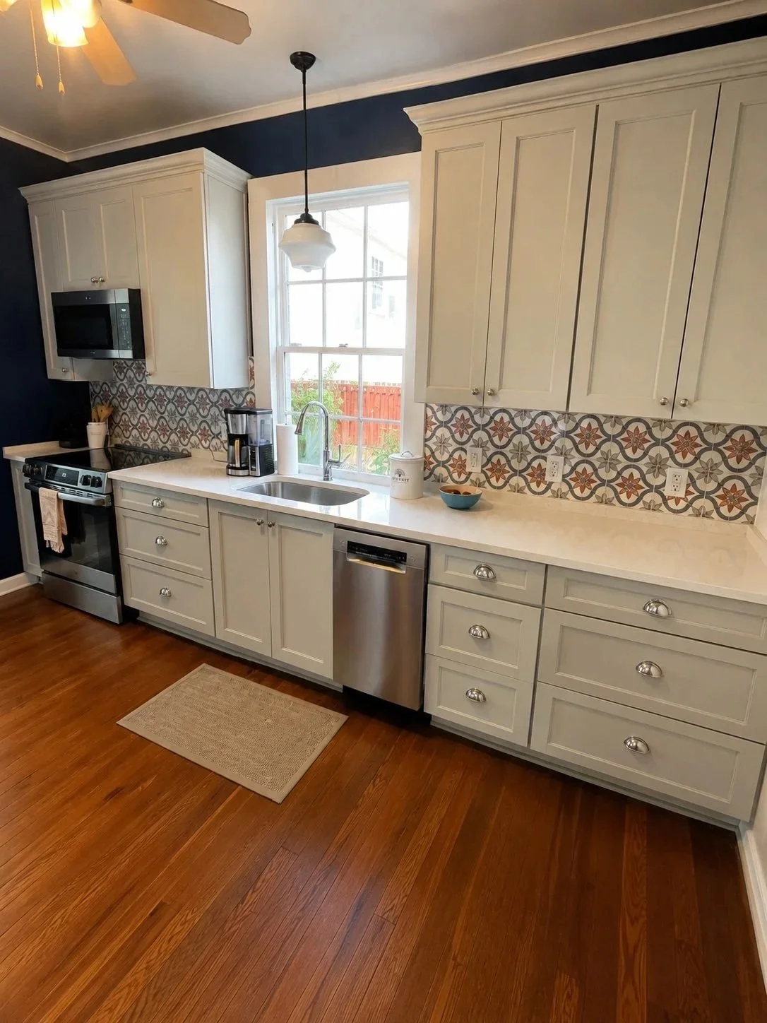 This completed kitchen renovation by Grand Rising Construction showcases custom shaker cabinetry, quartz countertops, a decorative patterned tile backsplash, stainless steel appliances, updated lighting, and a modern farmhouse sink. Serving Covington
