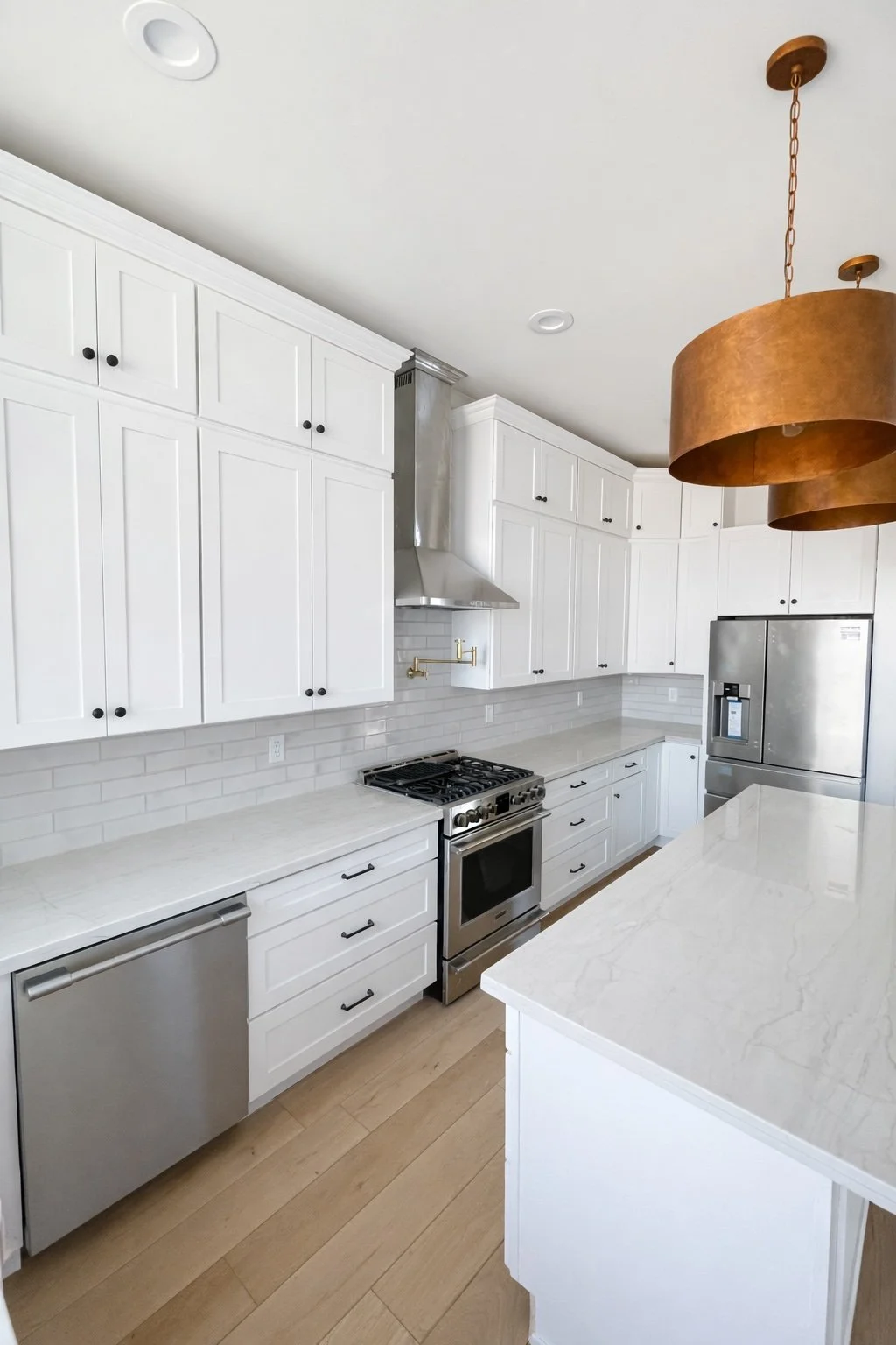 Completed kitchen remodel featuring white cabinetry, quartz island, stainless steel appliances, pendant lighting, and hardwood flooring.