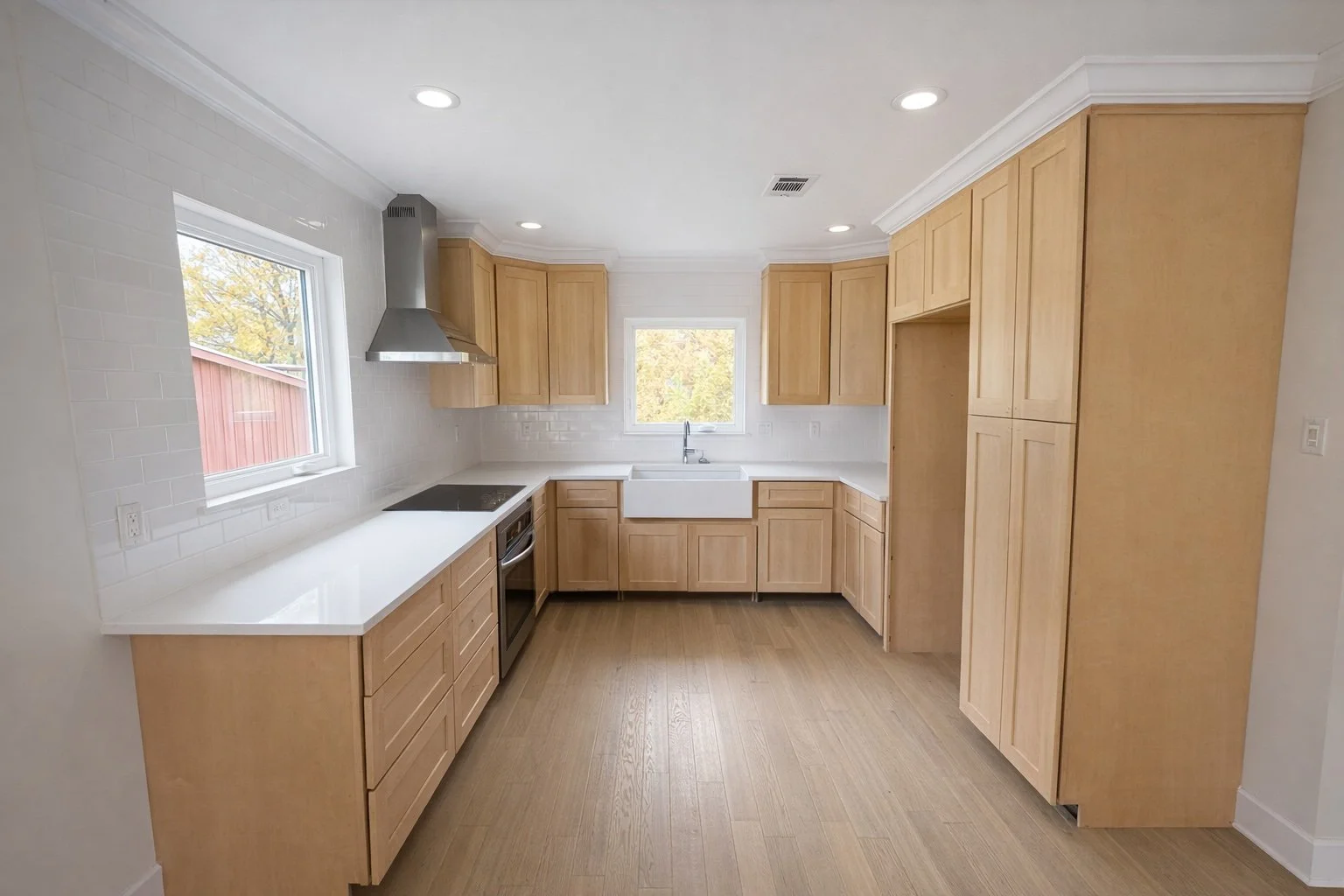 Bright, professionally remodeled L-shaped kitchen with custom wood cabinetry, quartz countertops, stainless steel appliances, and hardwood flooring.