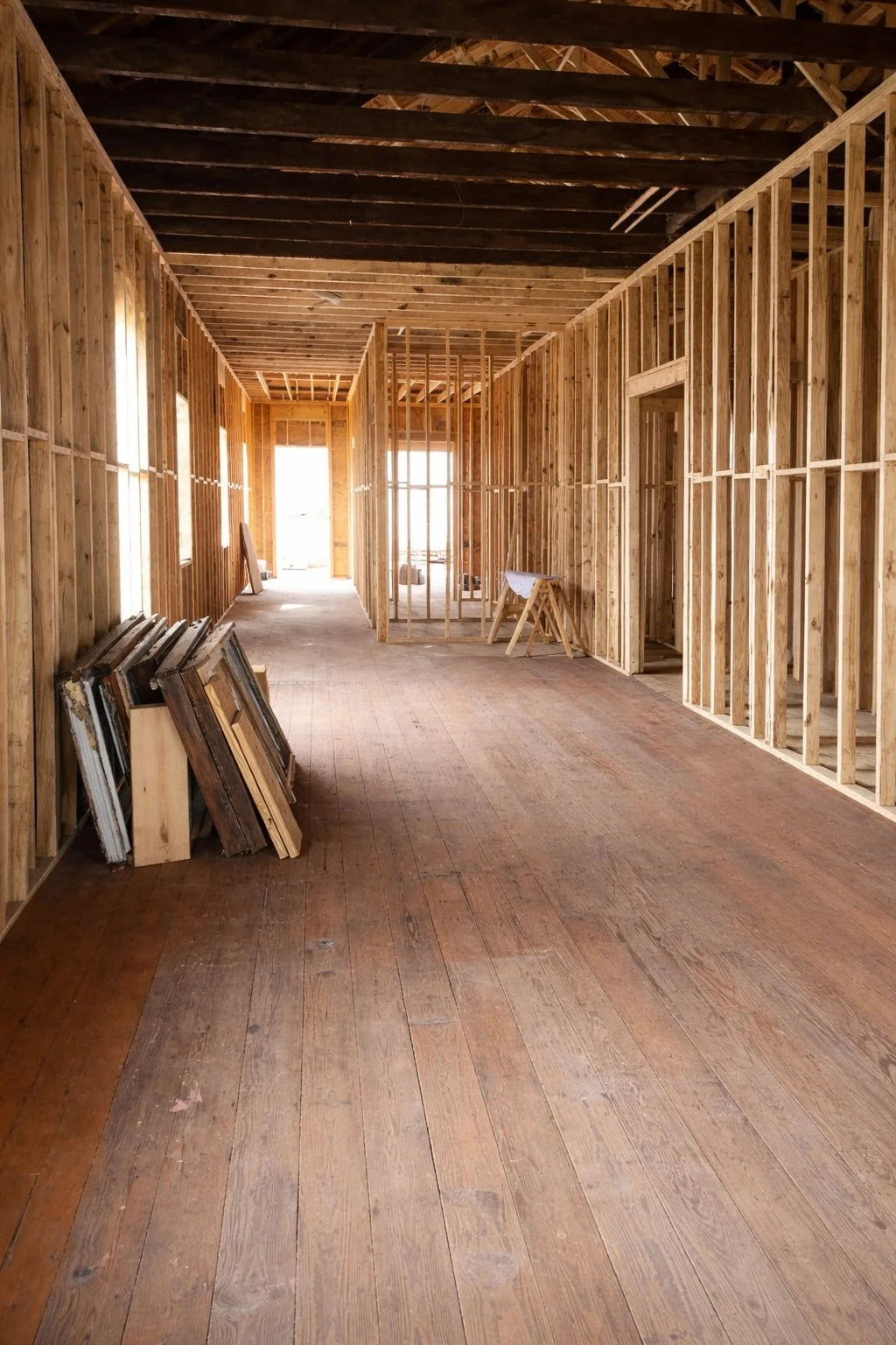 Interior residential renovation showing framing in progress with exposed studs and original wood flooring.