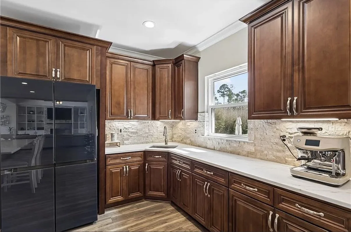 This luxury kitchen renovation by Grand Rising Construction showcases custom stained wood cabinetry, a handcrafted decorative range hood, quartz countertops, a natural stone backsplash, stainless steel professional-grade appliances, and wood-look por
