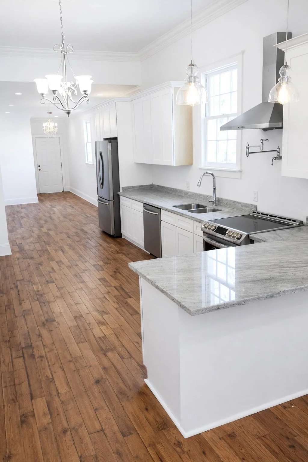 Completed galley kitchen remodel with white cabinetry, stone countertops, stainless steel appliances, and hardwood flooring.