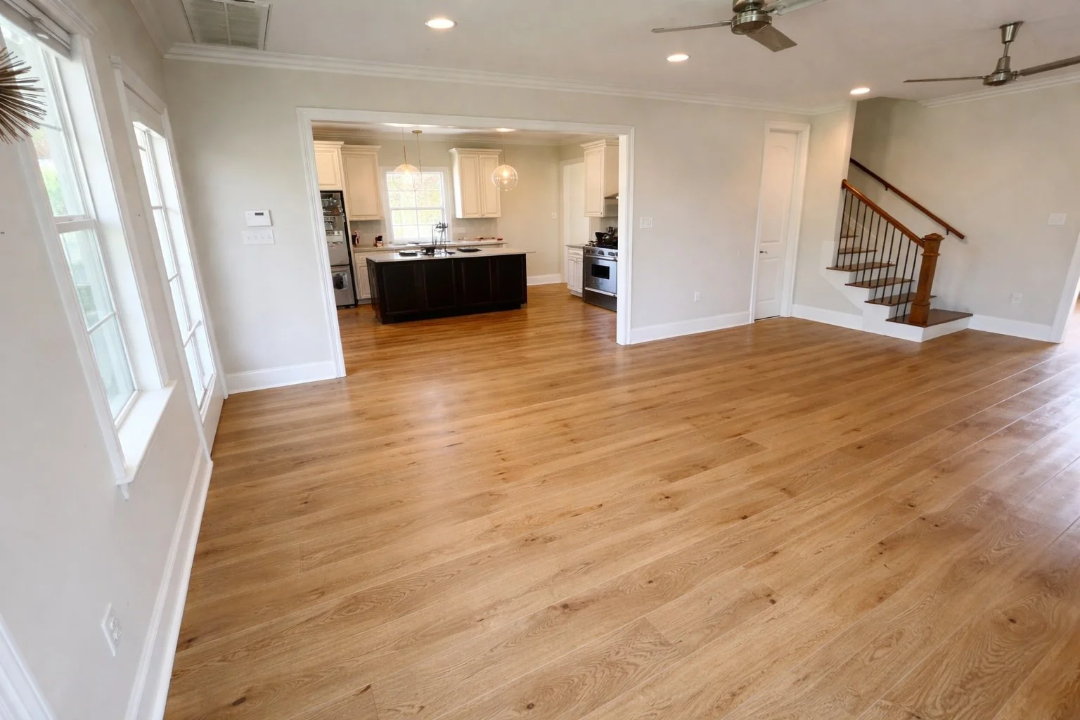 Wide-angle view of engineered wood flooring in a bright open-concept living area with seamless transitions and professional installation.