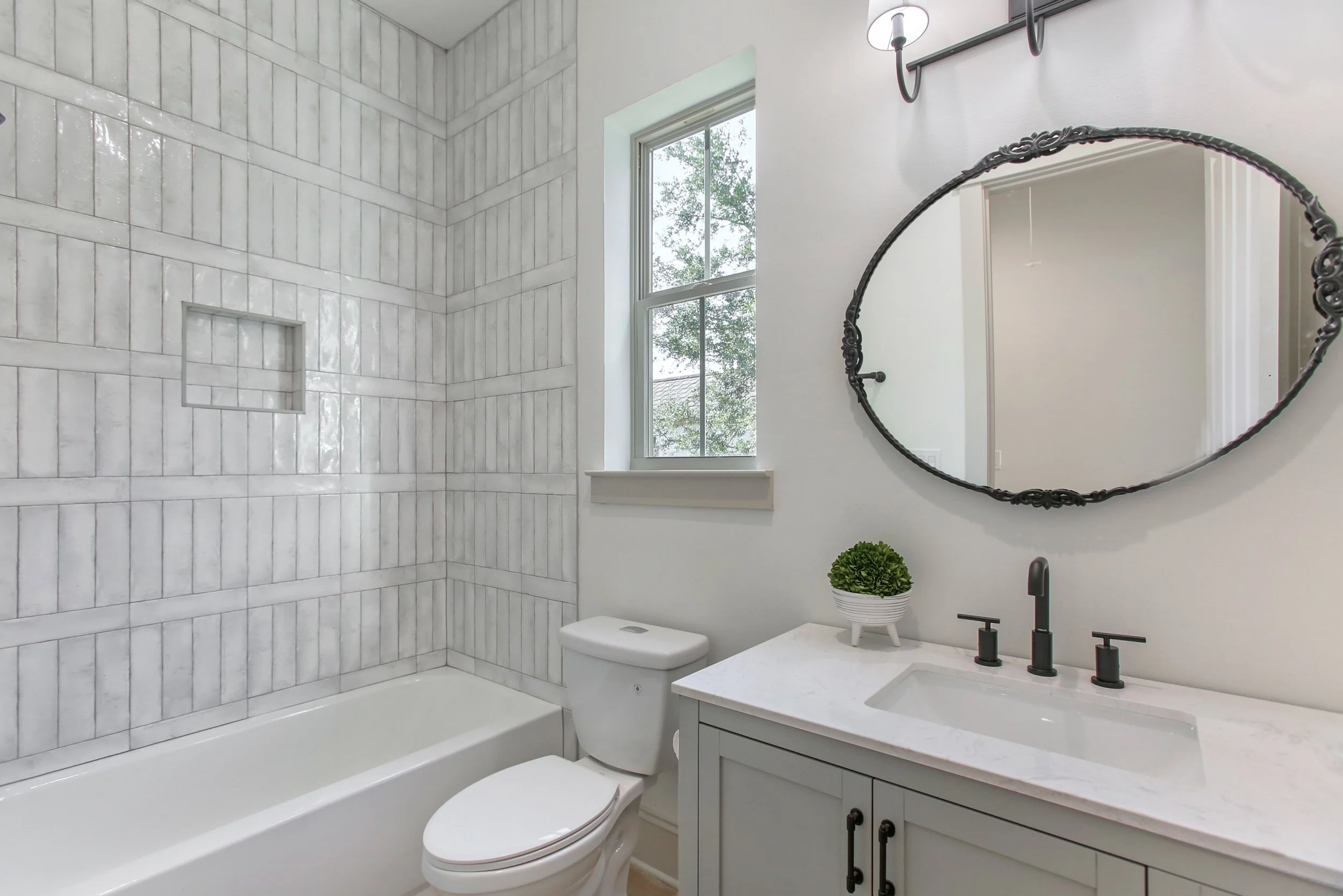 Bathroom remodel with vertical tile shower surround, built-in tub, custom vanity, and matte black fixtures.