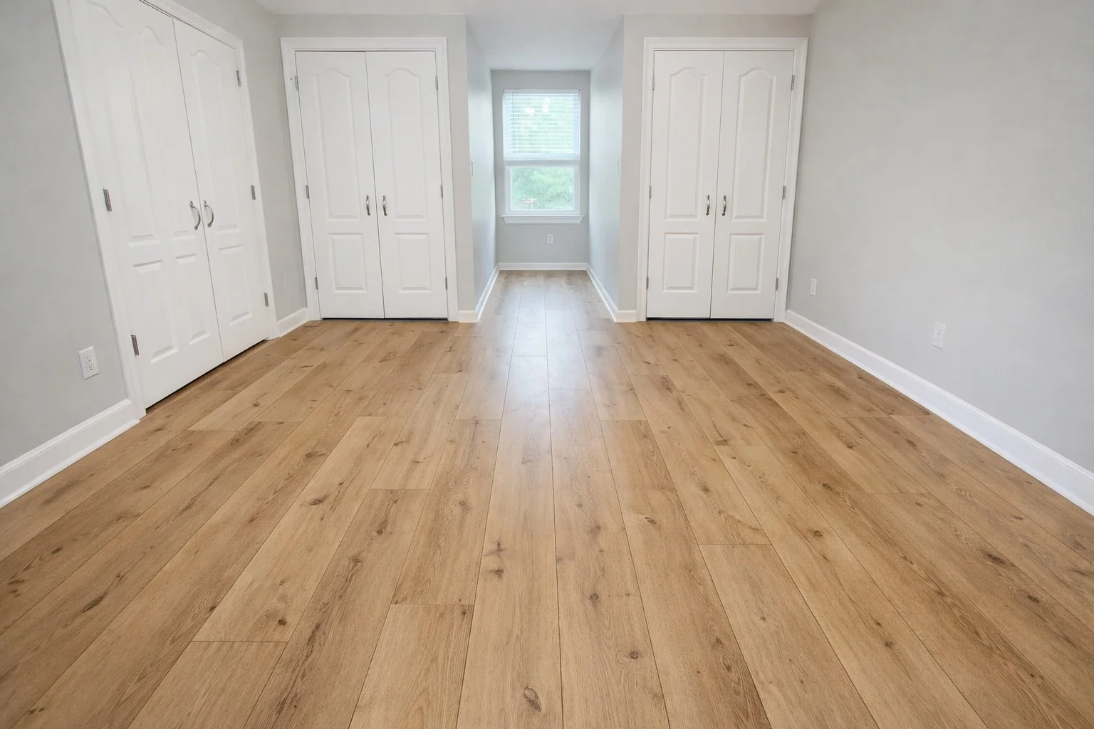 Wide-angle view of luxury vinyl plank flooring in a bright, unfurnished room with white trim and neutral walls in Covington, LA By Grand Rising Construction.