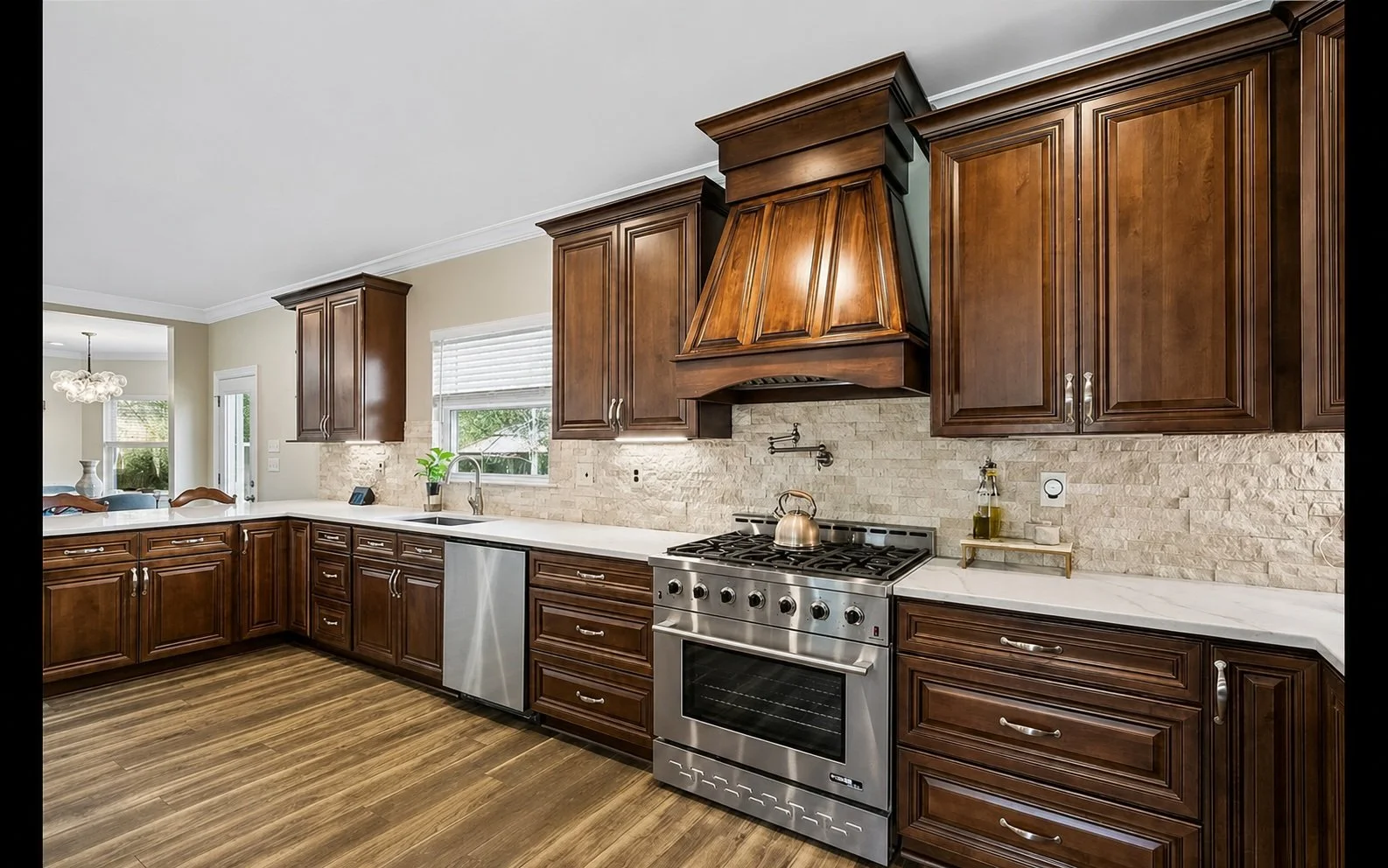 This luxury kitchen renovation by Grand Rising Construction showcases custom stained wood cabinetry, a handcrafted decorative range hood, quartz countertops, a natural stone backsplash, stainless steel professional-grade appliances, and wood-look por