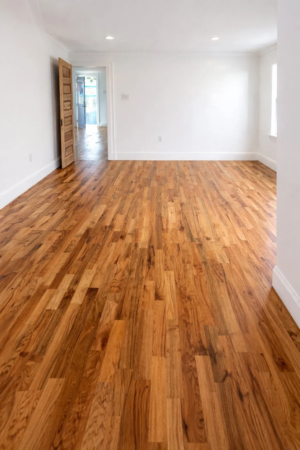 Wide-angle view of a bright finished room with newly installed white oak hardwood flooring, clean white walls, and professional craftsmanship.